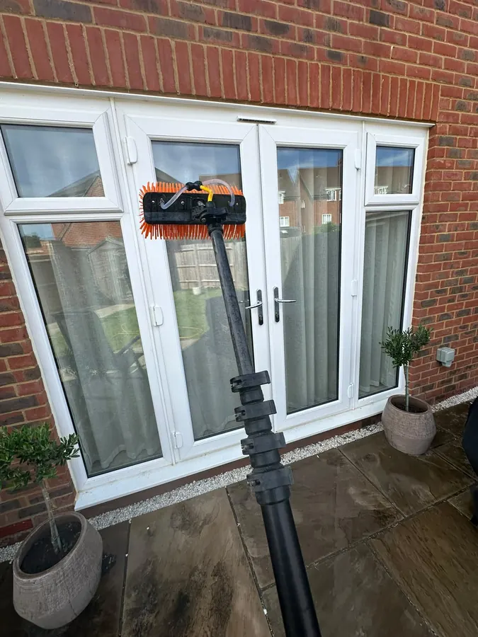 Water-fed pole brush cleaning glazed French doors on a red-brick home